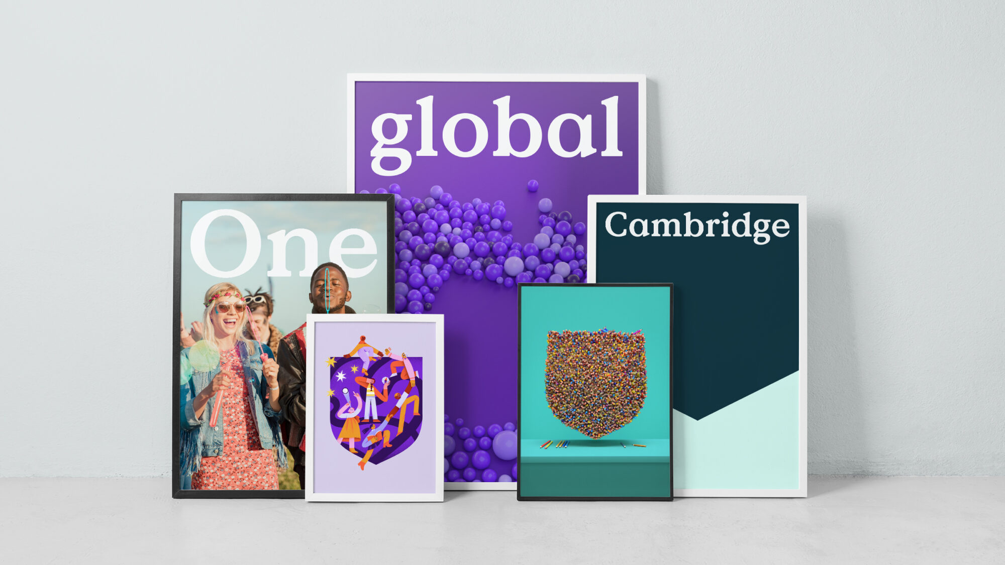 Five framed posters leaning on a wall showing different Cambridge marketing materials. The poster in the back shows the Cambridge logo and the text 