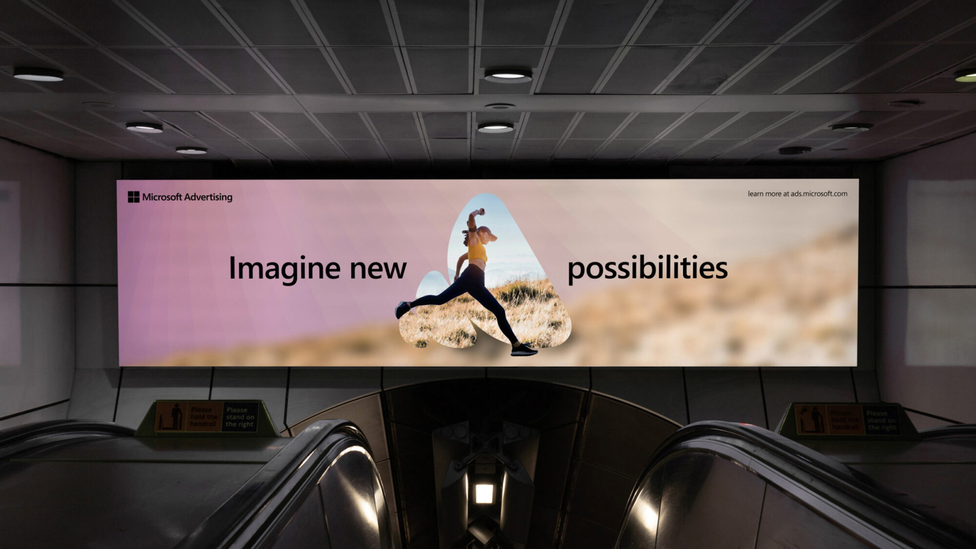 A large advertisement above escalators featuring a woman jumping in nature, masked into the Microsoft Advertising logo with the title “Imagine new possibilities”.