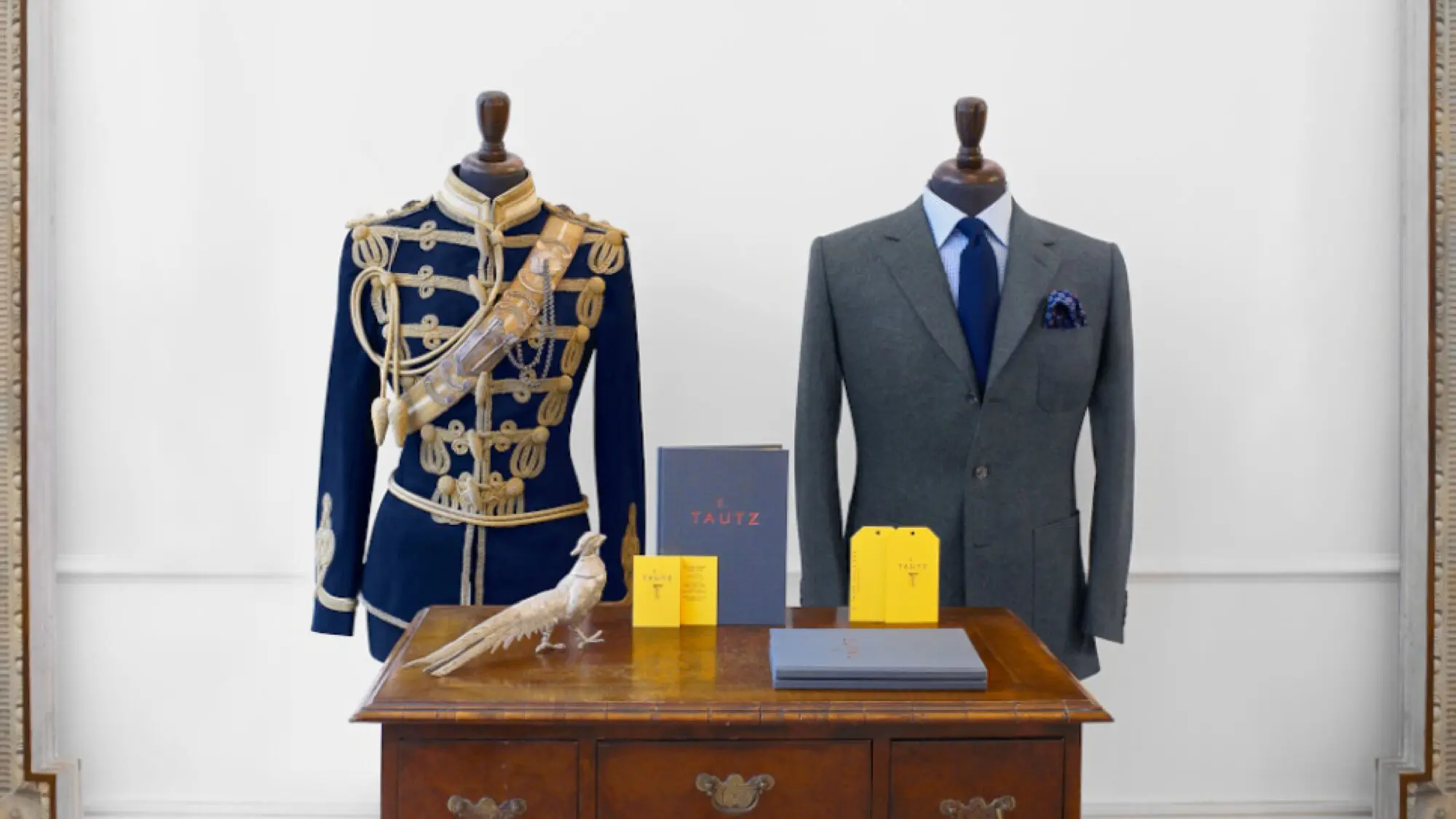 Two high-end E. Tautz suits on mannequins, one modern, one vintage military, behind a desk featuring the new brand in action.